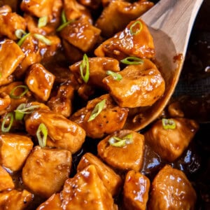 A serving spoon scoops out honey bourbon chicken from the pan for serving.