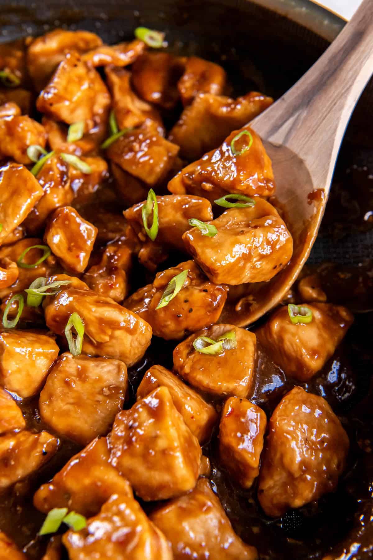 A serving spoon scoops out honey bourbon chicken from the pan for serving.