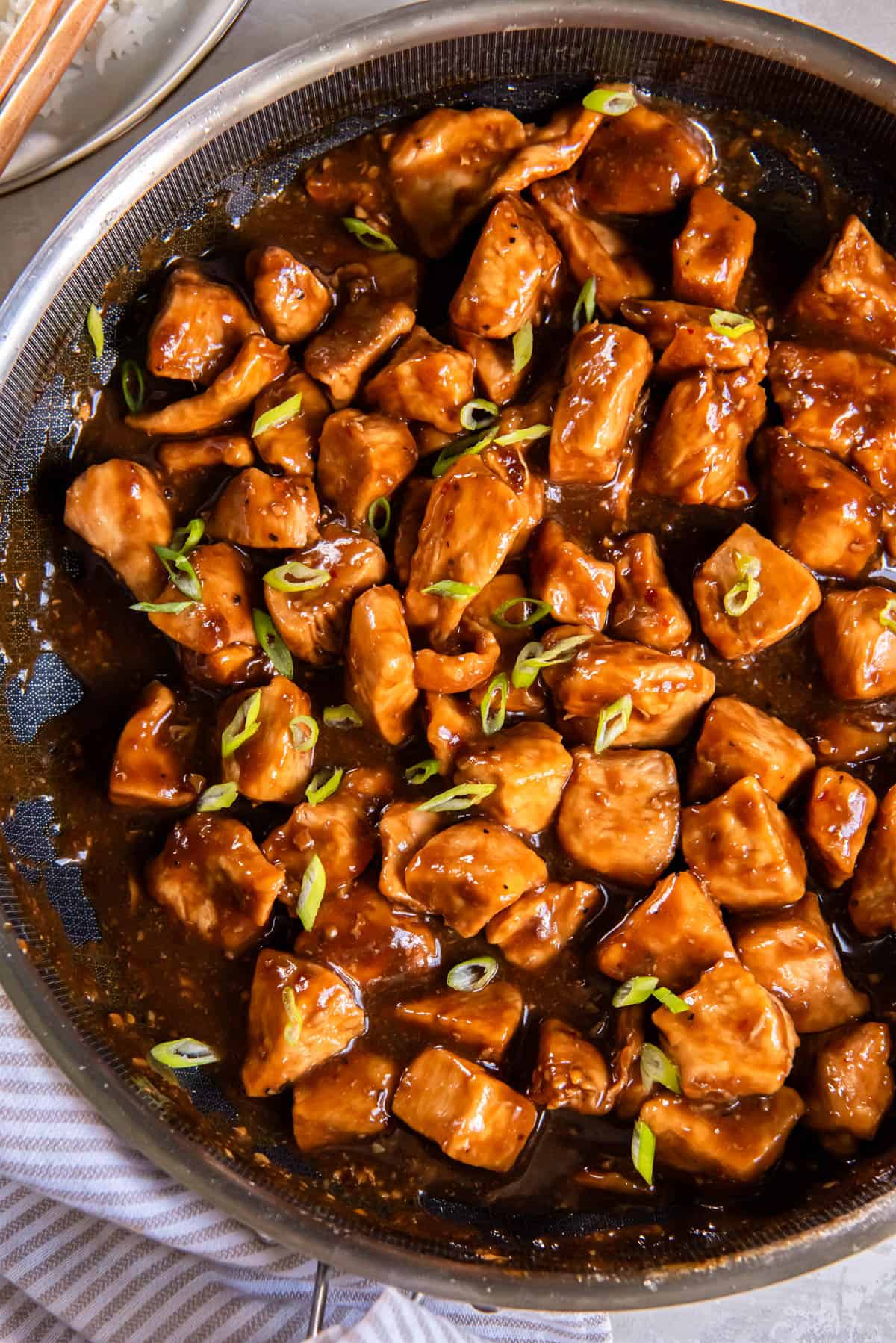 Honey bourbon chicken in a pan after cooking. The chicken is sprinkled with chopped green onion. 