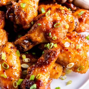 A pile of hot honey chicken wings on a white plate and sprinkled with chopped chives.