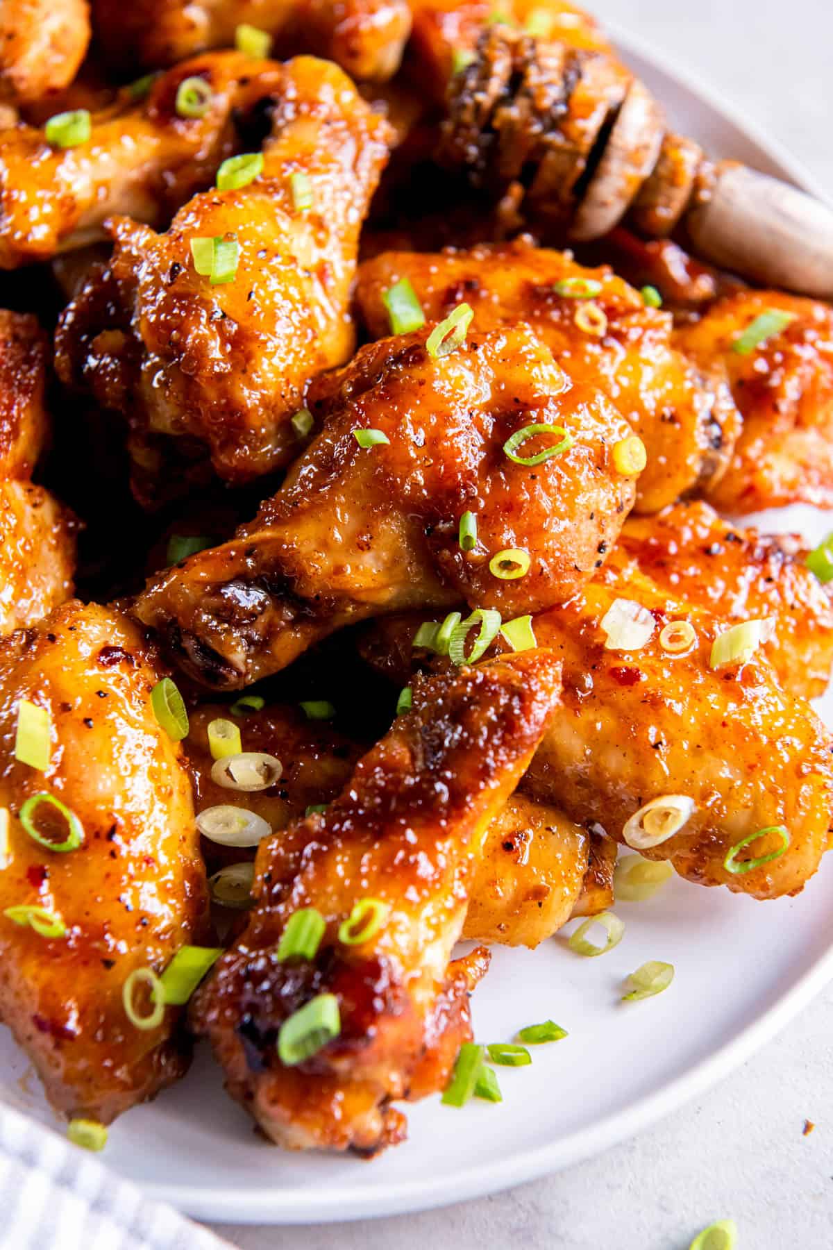 A pile of hot honey chicken wings on a white plate and sprinkled with chopped chives. 