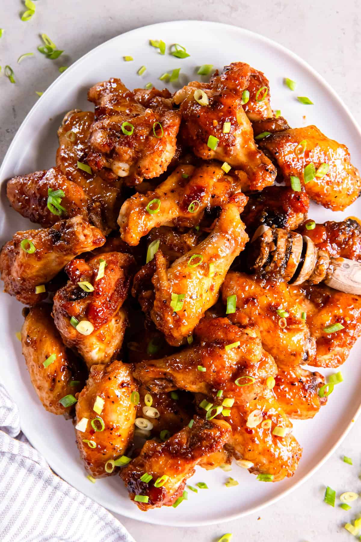 A white plate stacked with crispy baked hot honey chicken wings.