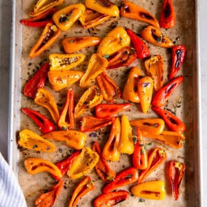 A sheet pan filled with roasted mini peppers sitting on a while countertop.