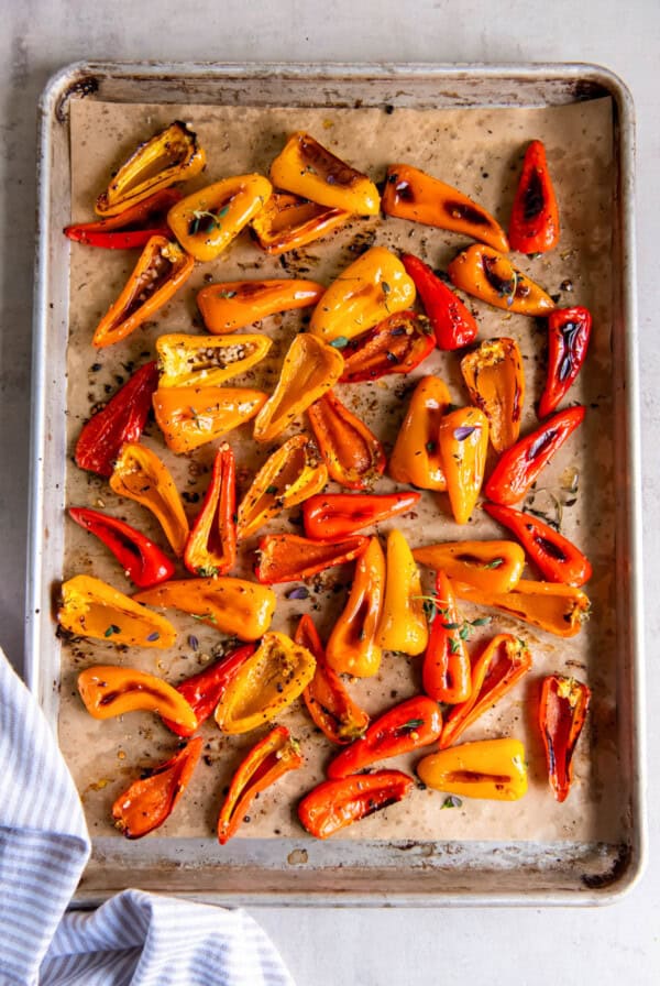 A sheet pan filled with roasted mini peppers sitting on a while countertop.