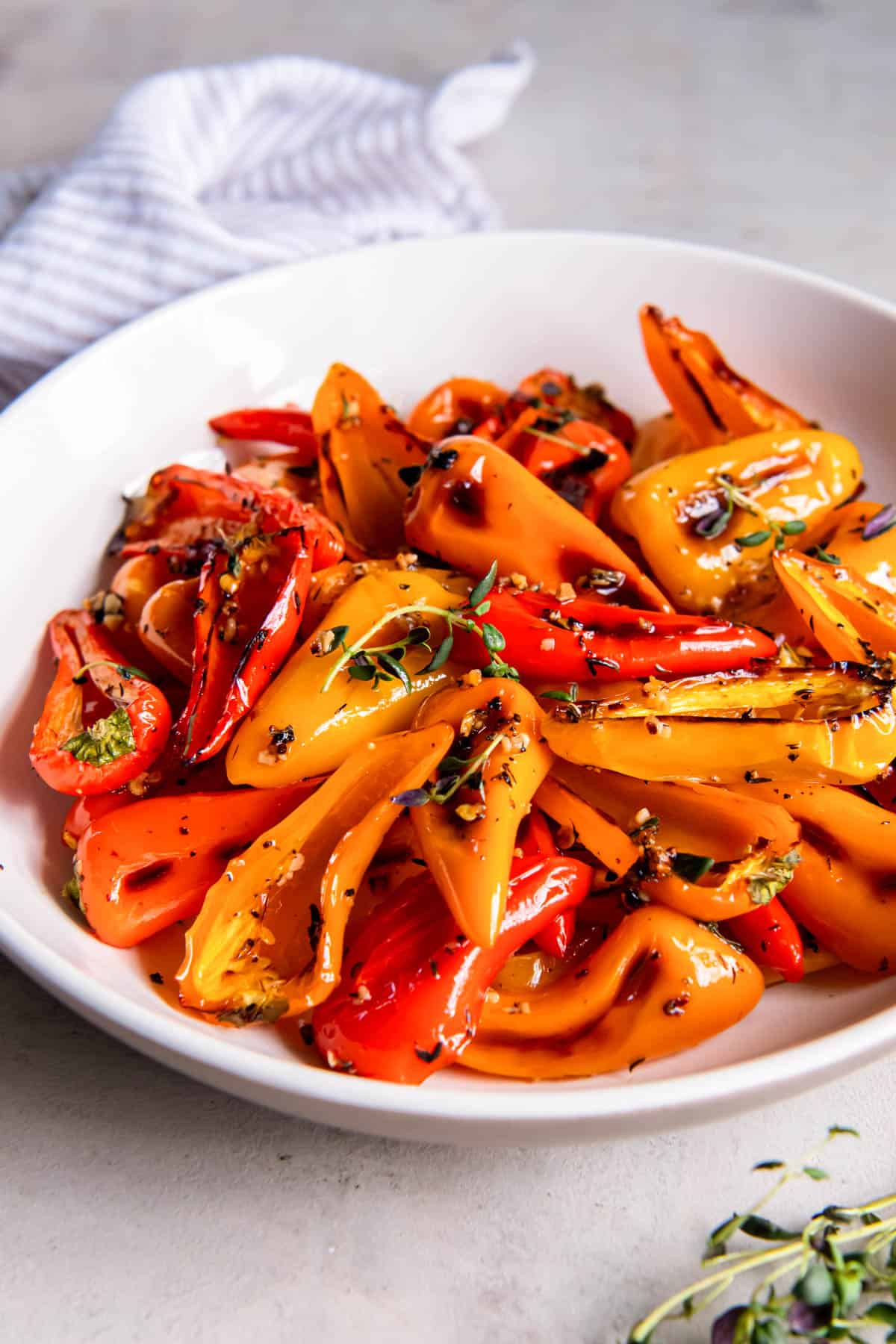 Roasted sweet peppers in a while bowl for serving. They are garnished with fresh thyme. 