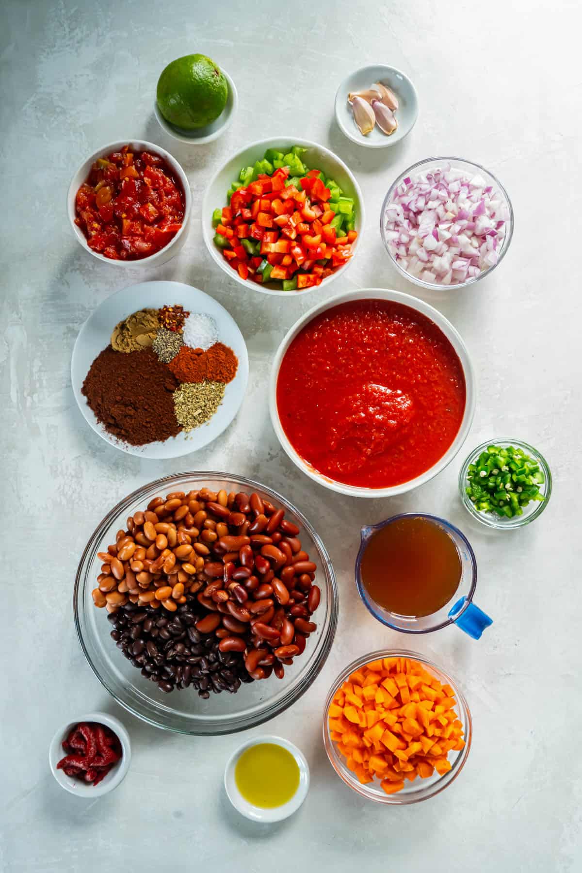 All of the ingredients for three bean chili in bowls on a white counter. 