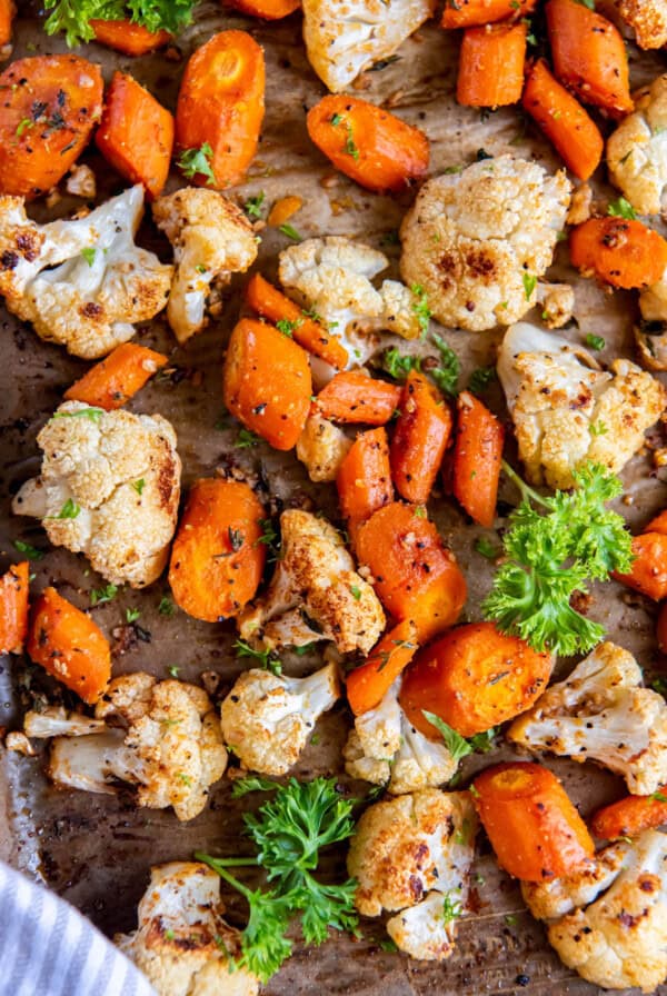 Roasted carrots and cauliflower on a sheet pan with fresh parsley for serving.