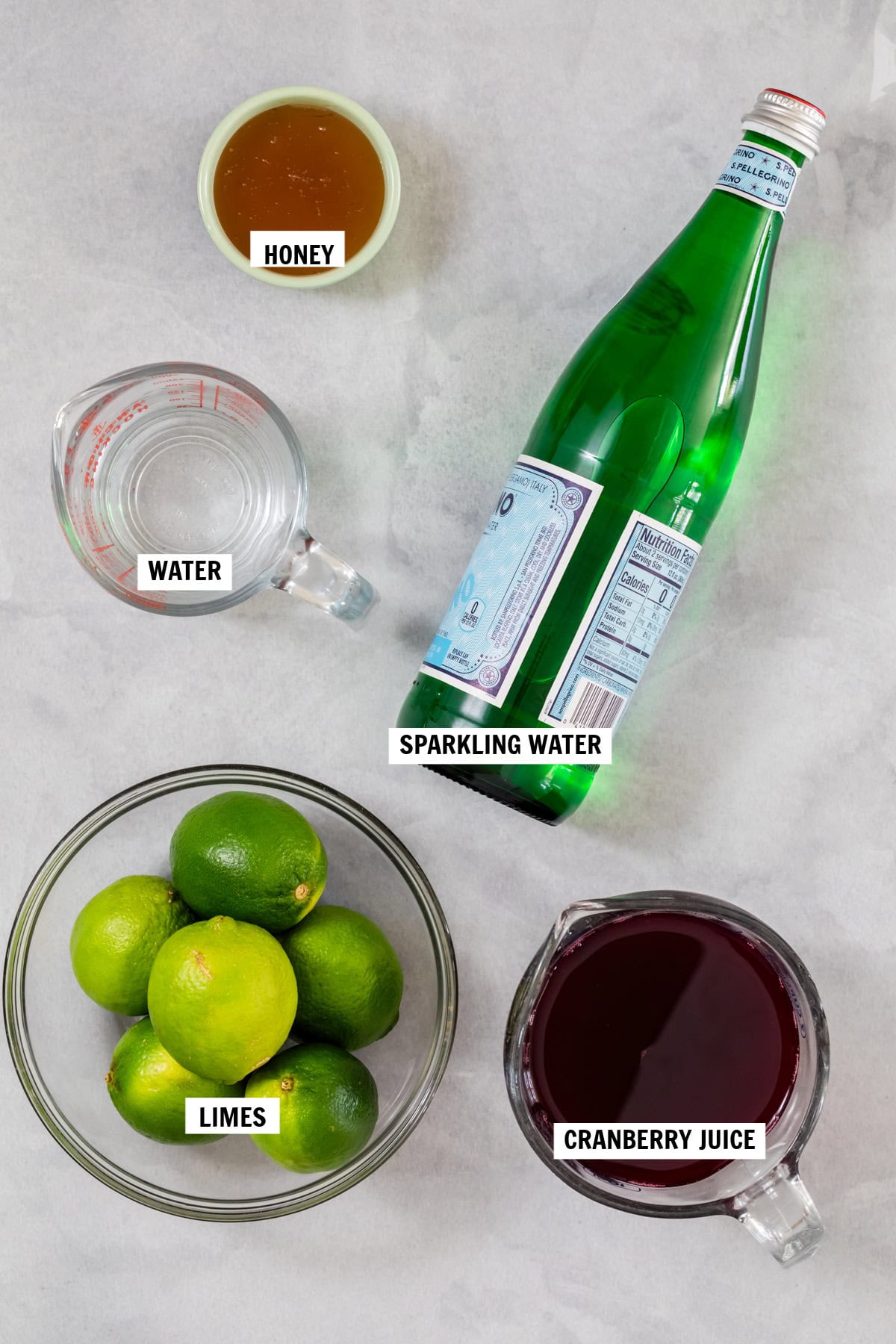 All of the ingredients for cranberry mocktail on a white countertop. 