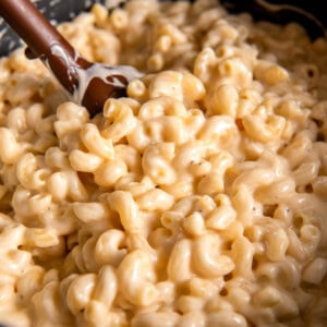 A large pot filled with creamy gouda mac and cheese. A wooden spoon scoops some of the mac and cheese out of the pot.