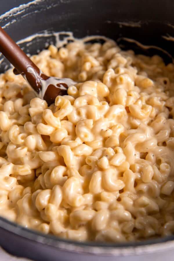 A large pot filled with creamy gouda mac and cheese. A wooden spoon scoops some of the mac and cheese out of the pot.