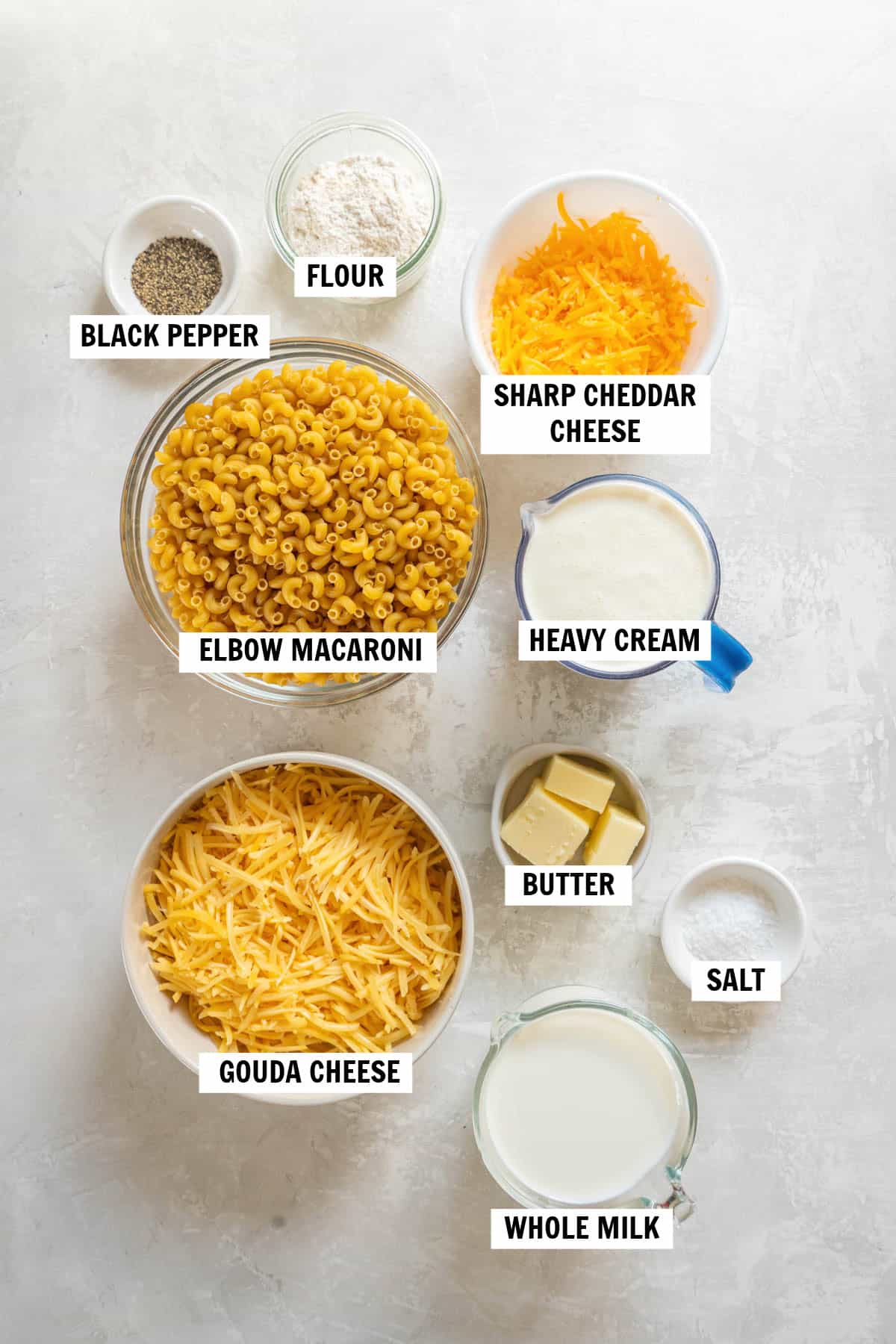 All of the ingredients for gouda mac and cheese in bowls on a white countertop. 