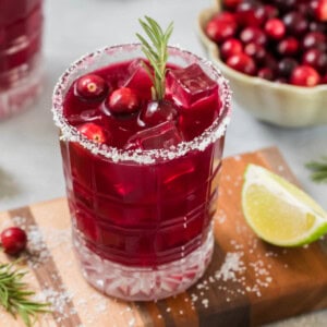 Sparkling cranberry mocktail in a glass on a small cutting board for serving.