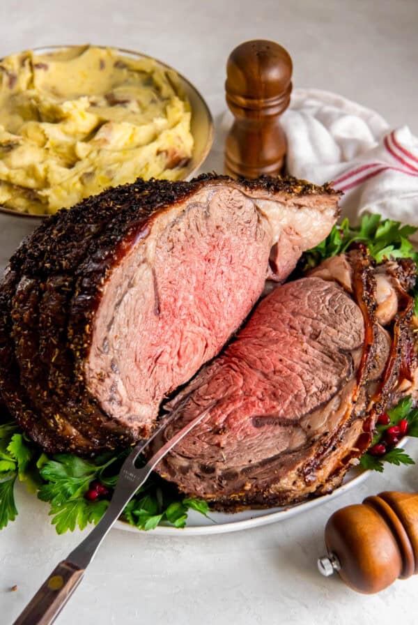 Slow roasted prime rib roast served on a festive platter, with a bowl of mashed potatoes behind it.