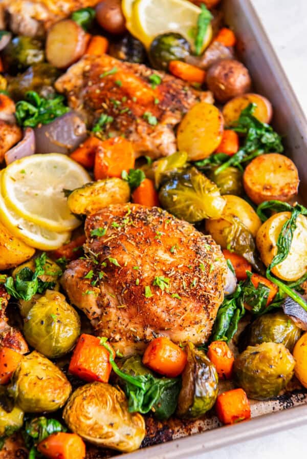 Sheet pan chicken thighs with vegetables like carrots, brussels sprouts, red onion and potatoes on a sheet pan after baking.