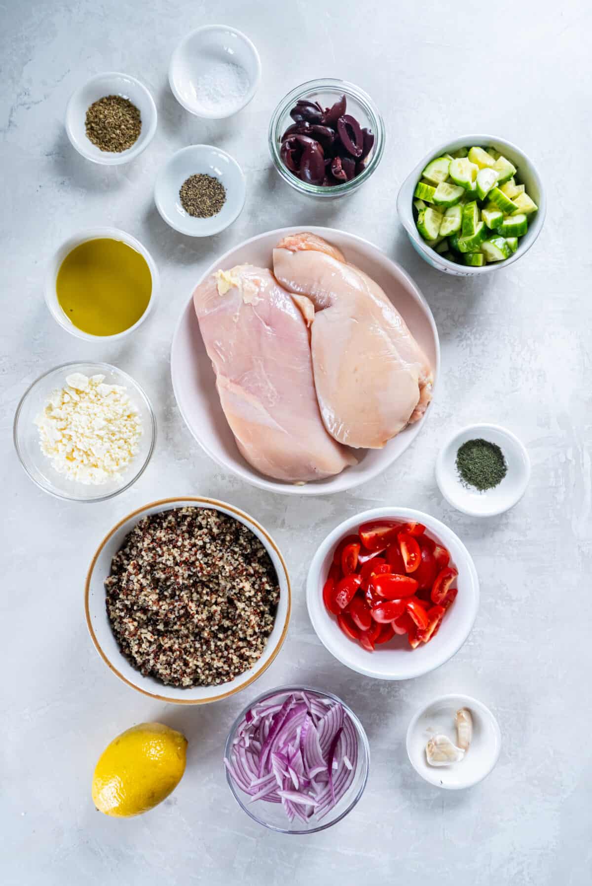 Ingredients for Mediterranean Chicken Bowl that include kalamata olives, cucumbers, tomatoes, red onion, quinoa, pita wedges, tzatziki sauce, and chicken.