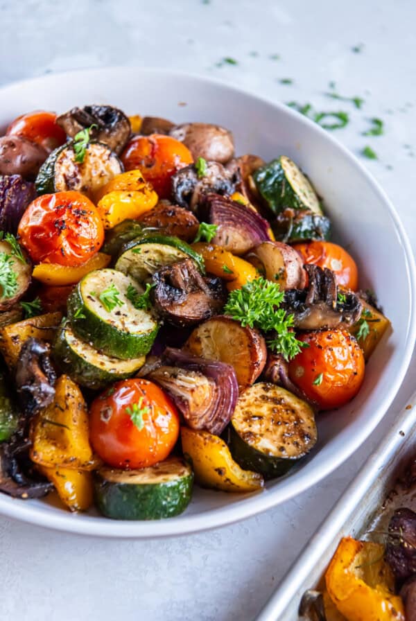 A bowl of roasted seasoned vegetables including zucchini, tomatoes, bell peppers, mushruooms and onions.