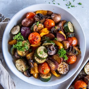 A bowl of roasted seasoned vegetables including zucchini, tomatoes, bell peppers, mushruooms and onions.