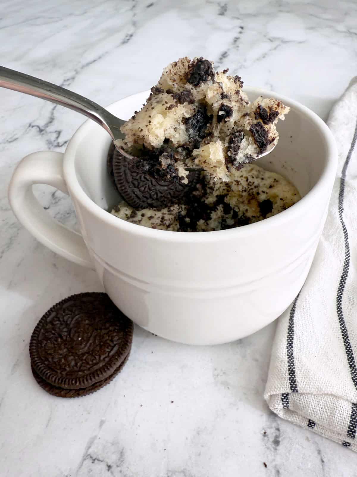 A mug with cake in it and a spoon scooping out a bite 